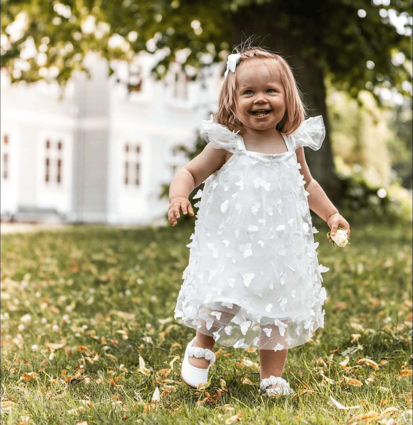 Liten flicka i vit klänning springer på gräsmattan
